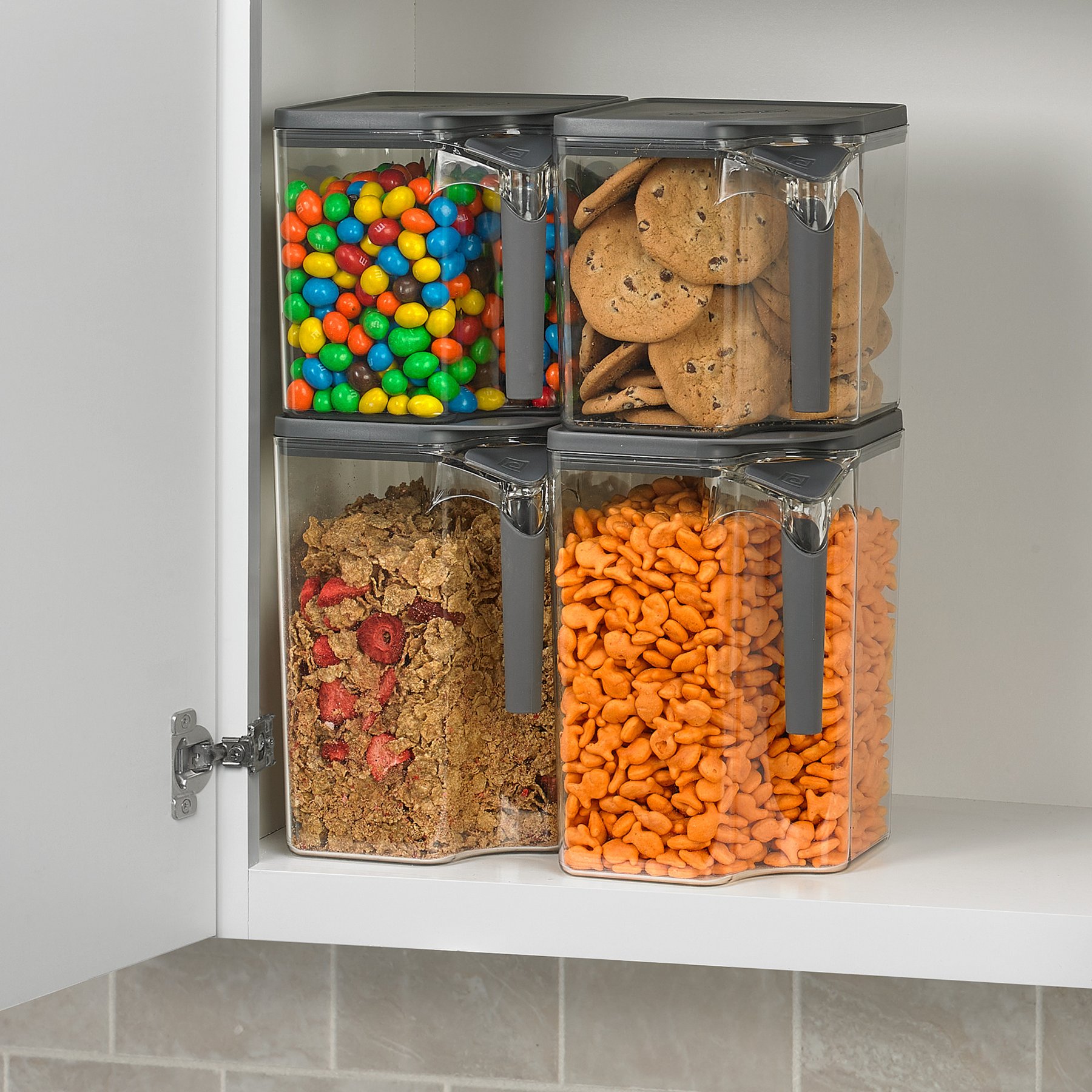 Handle-It canisters filled with candy, cookies, cereal and crackers, stacked in a pantry cabinet